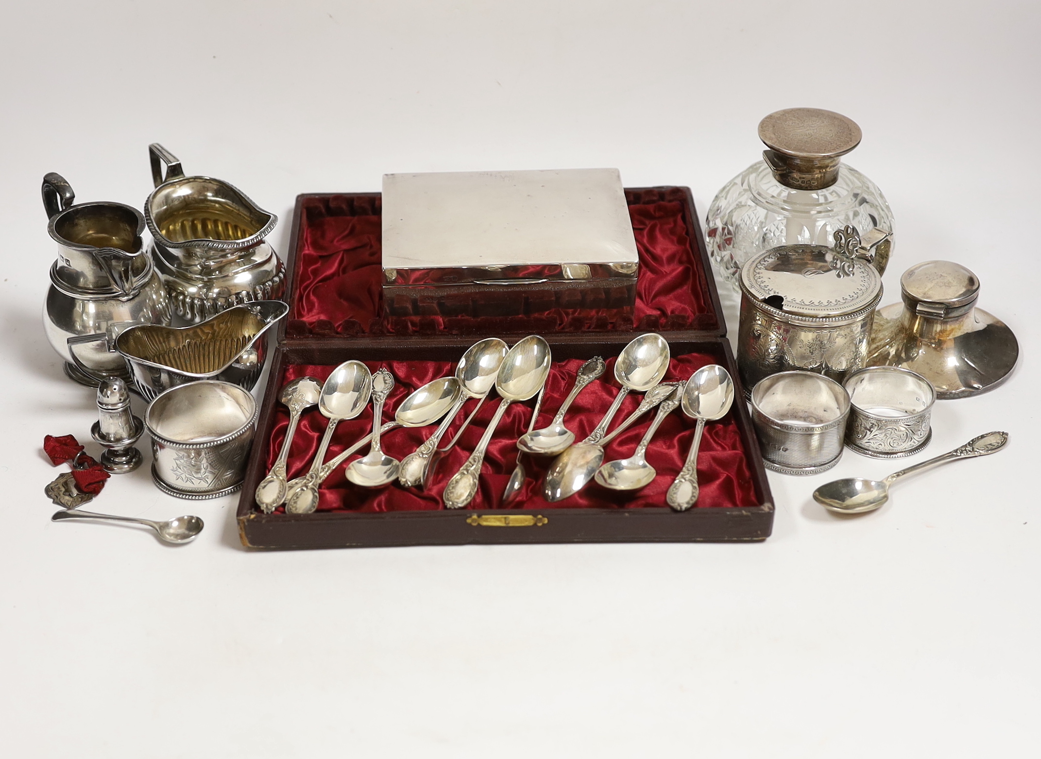 A Victorian silver mustard pot (no liner), a cased set of twelve silver teaspoons and tongs, two silver cream jugs, mounted glass scent bottle, napkin rings etc.